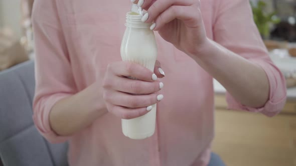 Close-up of Young Caucasian Woman in Pink Shirt Opening White Bottle of Yogurt