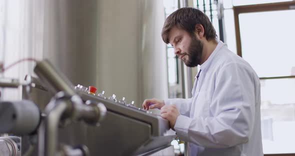 A Male Brewer with a Beard at Brewery Factory Working Behind the Control Panel Dashboard