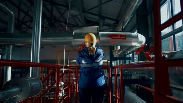 Woman worker in a factory in a helmet and uniform rotates a huge red valve