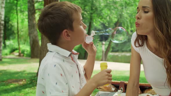 Boy Blowing Soap Bubbles in Forest. Mother Playing with Son in Summer Park