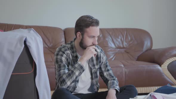 Portrait Handsome Bearded Man Sitting on the Floor and Packing Suitcases