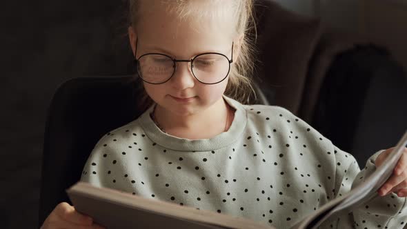 Little child clever girl reading a book in glasses after school, kid doing homework lessons