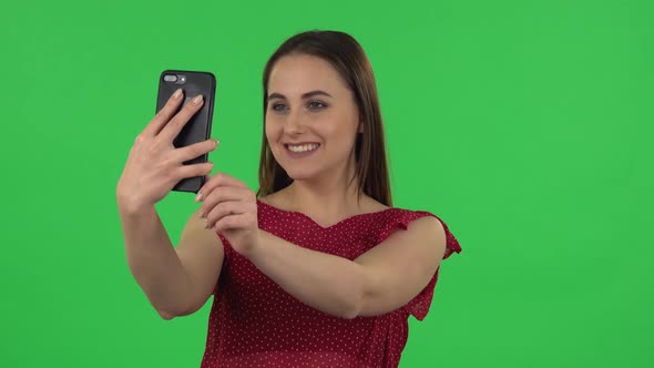 Portrait of Tender Girl in Red Dress Is Making Selfie on Mobile Phone Then Looking Photos. Green