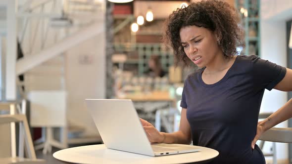 Young African Woman with Back Pain Using Laptop in Cafe 