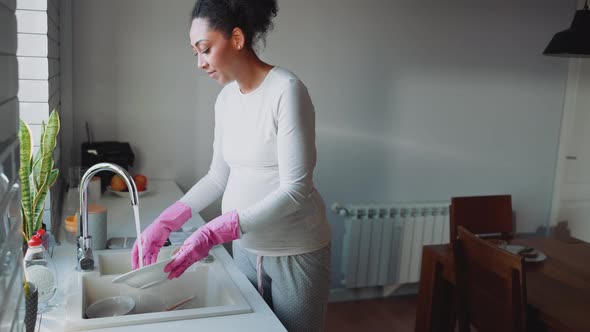 Positive African pregnant woman washing dishes