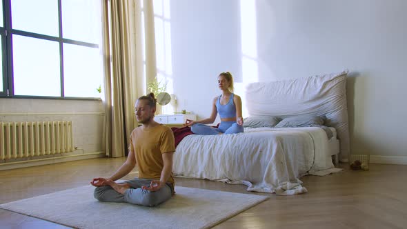 Young Couple is Meditating in Home Interior in Bedroom