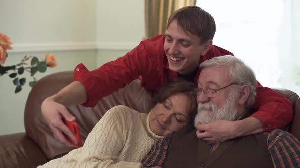 Cute Grandparents and Their Funny Grandson Are Doing Selfie, Looking at Smartphone Camera, Smiling