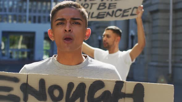 Two mixed race men on a protest march holding placards raising hands and shouting