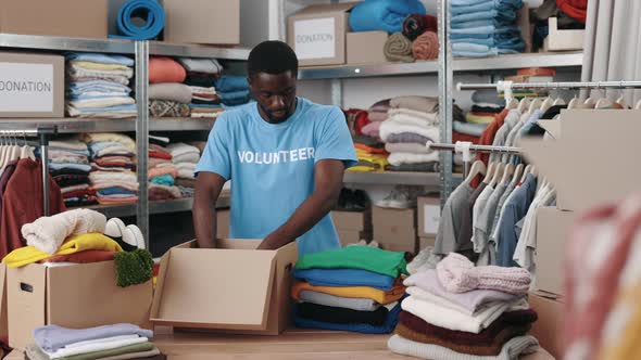 African American Man Standing at the Warehouse While Sorting and Iterating Clothes for Donations