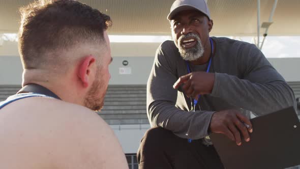 African american male coach and caucasian male athlete sitting and talking