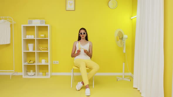 Young Woman Is Peeling Banana In Yellow Office