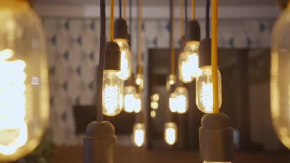 Live Camera Moves Along Row of Illuminated Lamp Bulbs Hanging Indoors