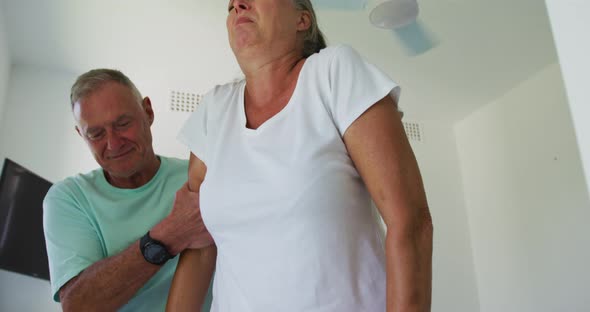 Caucasian senior man helping his wife walk using walking frame at home