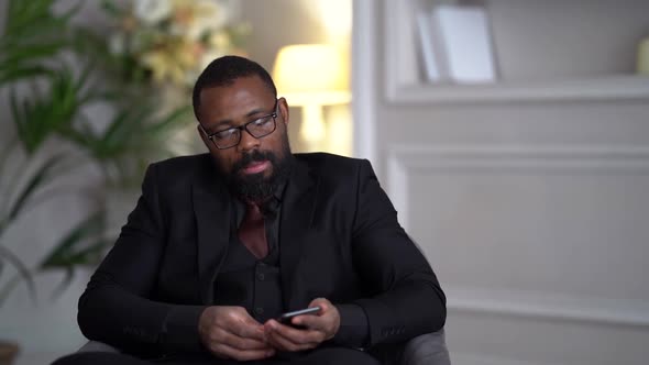 African-American Bearded Man in a Black Suit, Shirt, Stylish Glasses. A Businessman Is Working