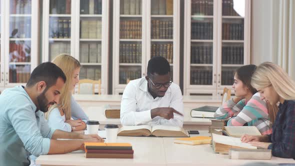 Multiethnic Young People Sitting at Table Reading Reference Books for Study Notes