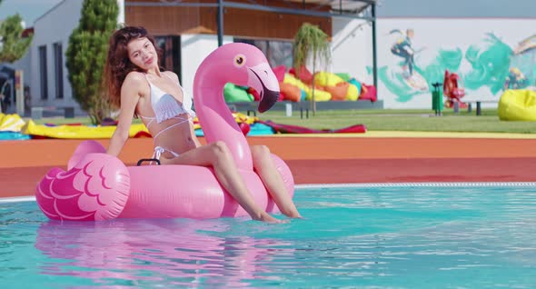 Woman in Swimsuit Swimming in Pool on Inflatable Flamingo