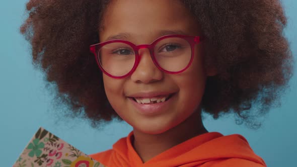 African American school girl in eye glasses writing with pencil in notebook and smiles at camera