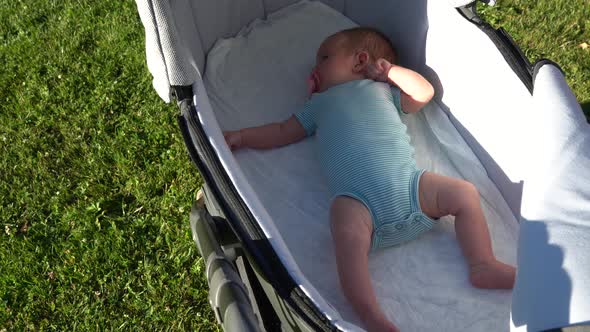 a Baby Caucasian Child with a Pacifier in His Mouth Relaxes Lying on His Back