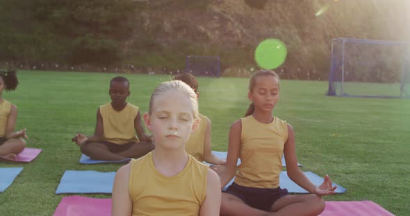 Diverse group of schoolchildren sitting on mats meditating during yoga lesson outdoors