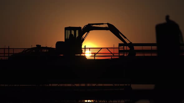 Silhouette of the Excavator on the Bridge with Passing Cars