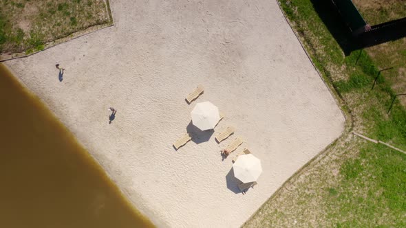 People Taking Rest at the Beach Area with Sand and Loungers Near a Small Lake in a Cottage Village