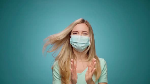 Woman in Medical Mask on Face is Very Happy and Claps Her Hands Against Blue Background