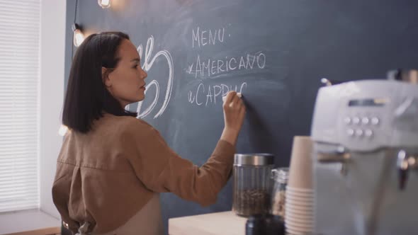 Asian Coffeeshop Worker Writing On Blackboard