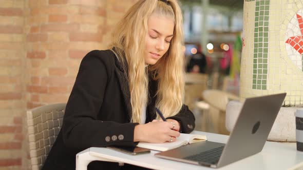 Freelancer woman writing notes while working with laptop in cafe