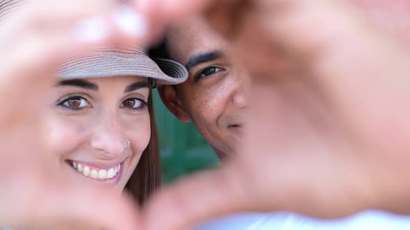 Mixed race couple do heart sign with hands, looking to camera - love and relationship