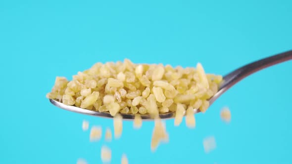 A full metal spoon of uncooked bulgur grains. Falling cereal in slow motion. Macro