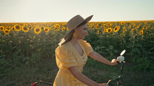 Free Woman in Long Dress Riding Retro Styled Bicycle on Country Road Near Sunflowers Field