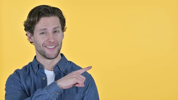 Young Man Pointing at Product and Talking on Yellow Background