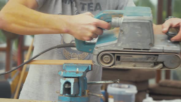 Belt sanding wooden teak trim with belt sander young caucasian male