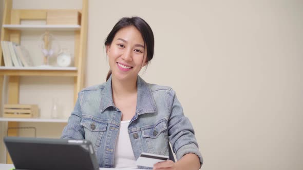 Asian woman using tablet buying online shopping by credit card while wear casual sitting on desk.