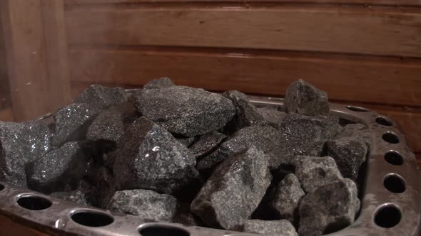 Water pouring over steaming hot coals in sauna, slow motion close up