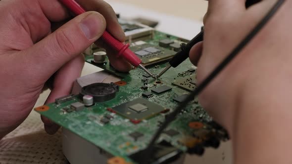 Close-up of Technician Man Measuring Electrical Voltage of Computer Mainboard.