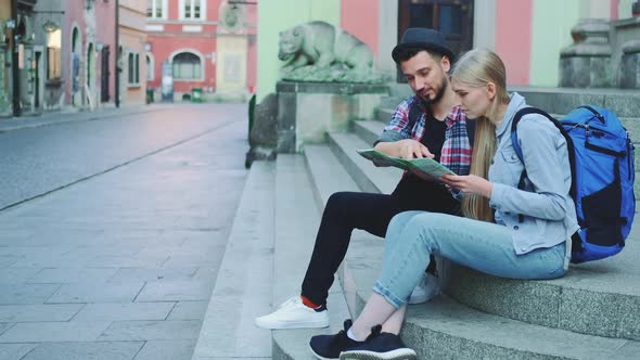 Tourist Couple Sitting on Street Stairs Checking City Map and Discussing