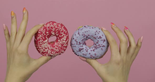 Womens Hands Holding Two Red and Blue, Sprinkled Donuts on Pink Background.