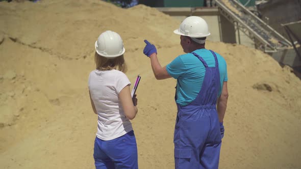 Back View of Male Worker and Female Inspector Standing in Front of Stack of Yellow Sand and Talking