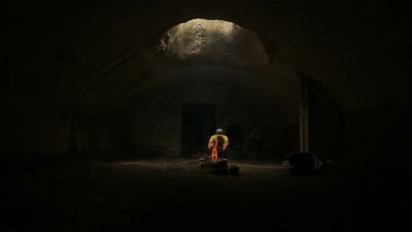 Young Man Stoking Fire in Underground Hut