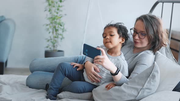 Young Mother with Her Son Use a Smartphone and Applications for Entertainment and Watching Videos 