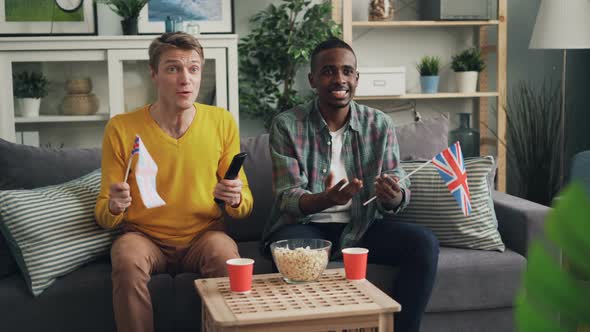 Excited Young People Are Supporting British Team Watching Sports Game on TV and Waving Flags