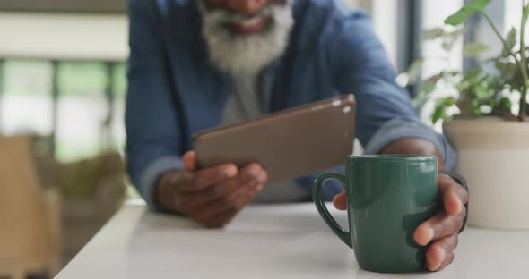 Video of african american senior man drinking coffee and using tablet