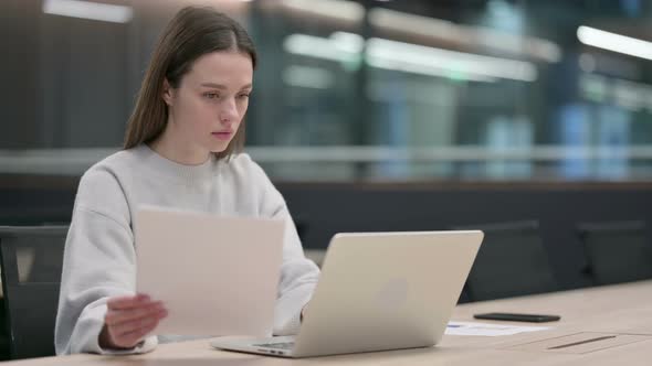 Woman Reading Documents while working on Laptop