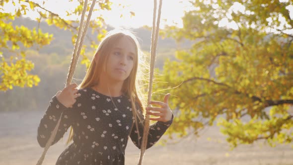 Happy Child Girl on Swing at Golden Sunset