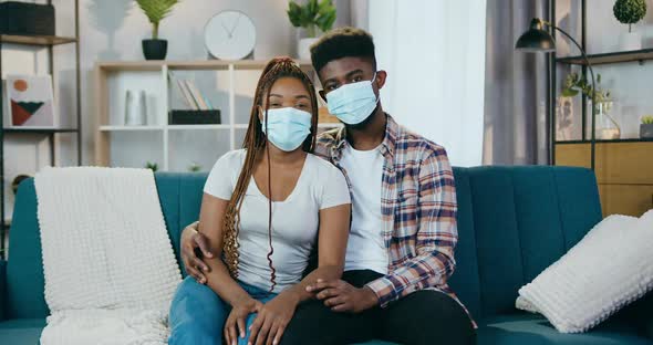 African American Couple Sitting on Couch in Medical Masks