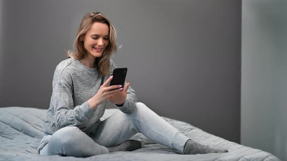 Smiling Female in Domestic Pajama Surfing Internet Use Smartphone on Bed