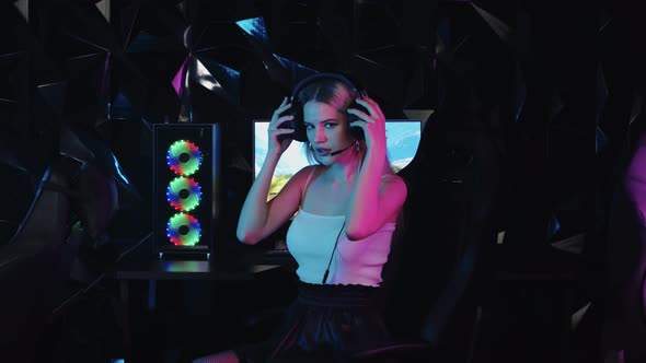 Young Blonde Sexy Gamer Girl Putting on Headphones and Starts Playing the Game