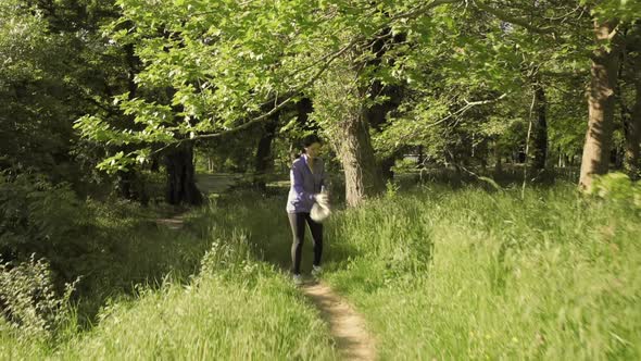 A Young Happy Woman Jogging at the Park and Collects Garbage