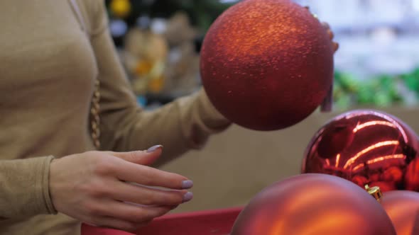 Young Woman Hands Take Glittering Bauble of Red Colour